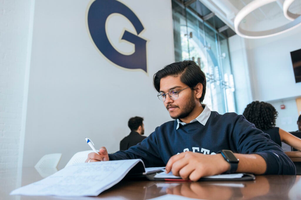 Man studying at a table. Prominent Georgetown logo in the background